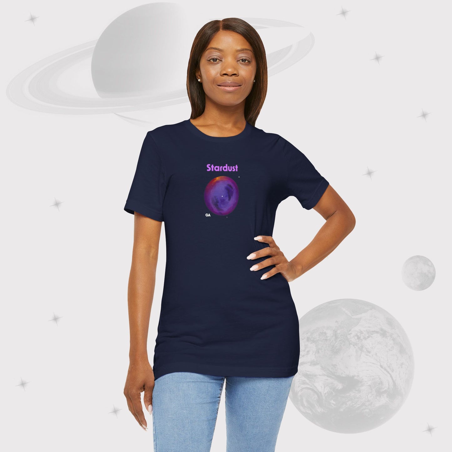 Woman wearing Going Across women's basic t-shirt in navy with jeans, featuring the text ‘Stardust’ with space art of bright purple nebula by Manharleen.