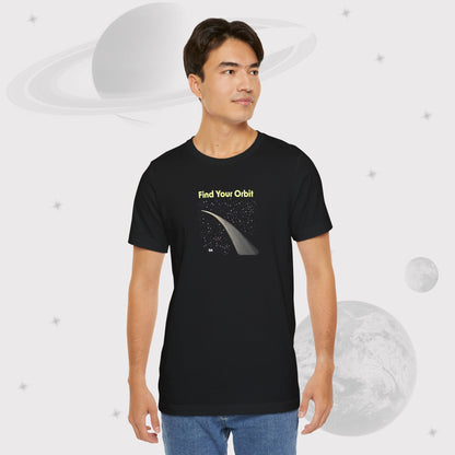 Guy wearing Going Across men's basic t-shirt in black with jeans, featuring the text ‘Find Your Orbit’ and space art of an orbit and a starry sky by Manharleen.