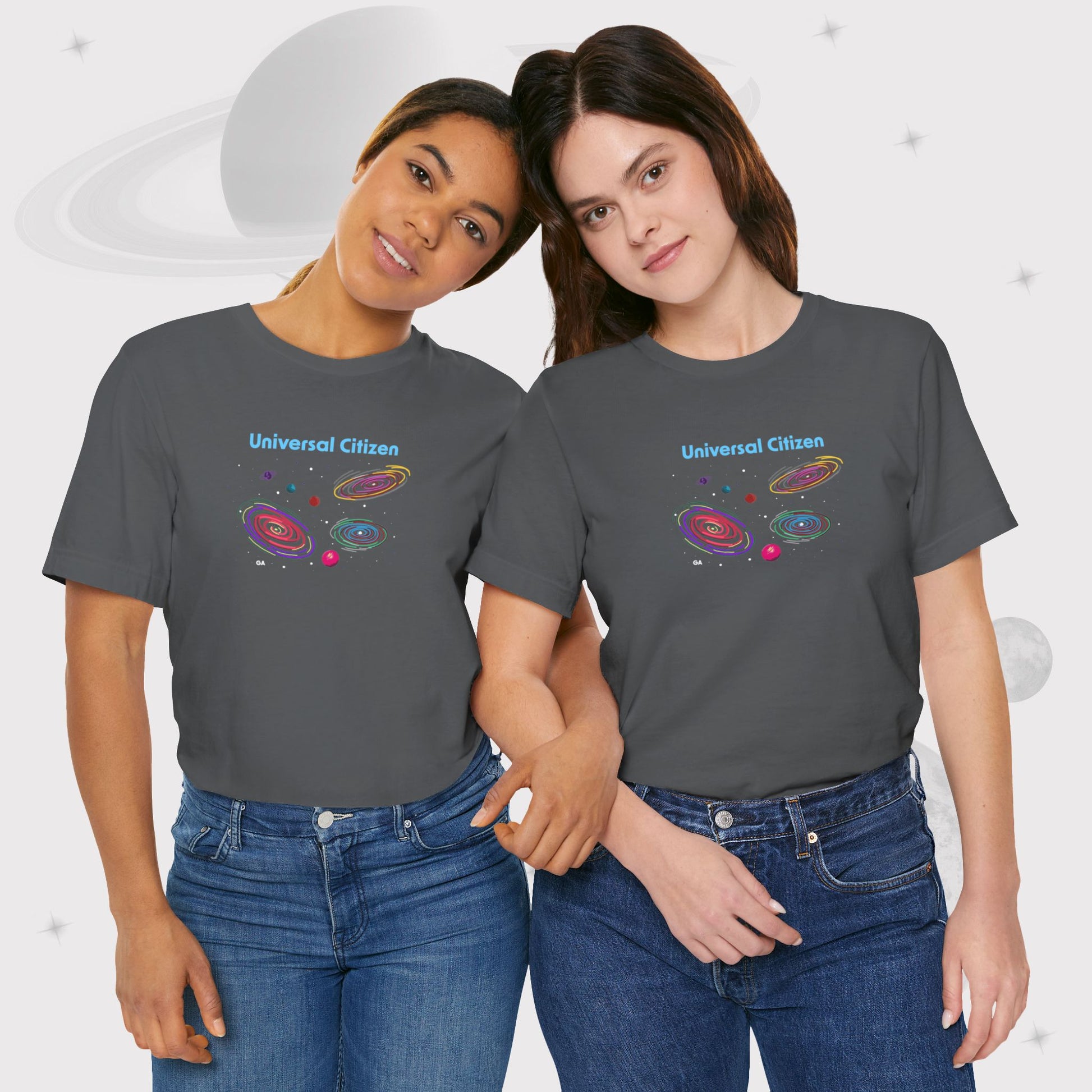 Two women wearing Going Across women's basic t-shirt in asphalt/gray, featuring the text ‘Universal Citizen’ with space art of vibrant galaxies and planets by Manharleen.