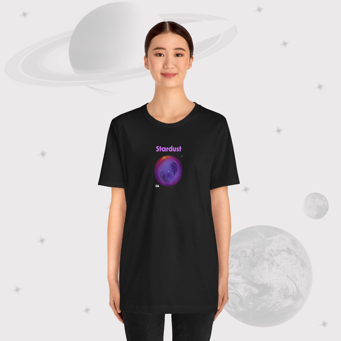 Woman wearing Going Across women's basic t-shirt in black with pants, featuring the text ‘Stardust’ with space art of bright purple nebula by Manharleen.