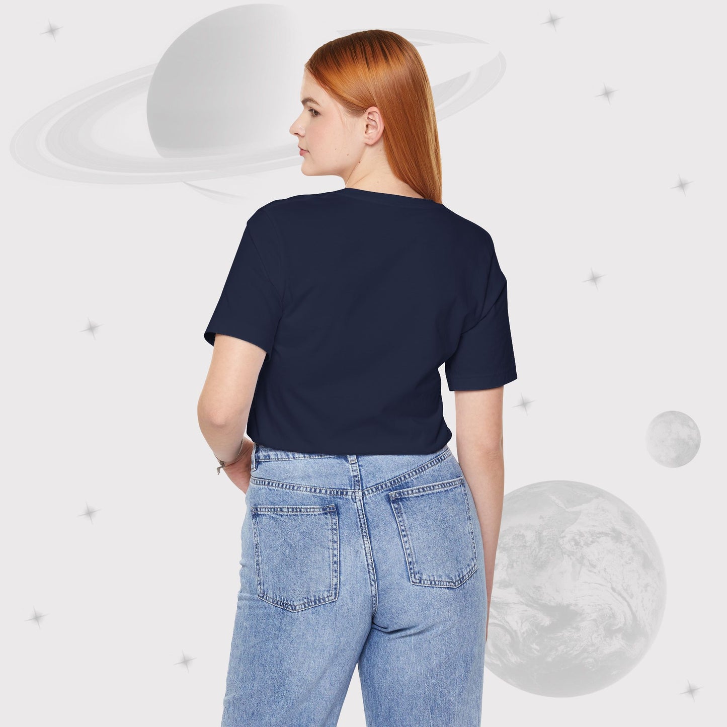 Back side of a woman wearing Going Across women's basic t-shirt in navy with high waist jeans, featuring the text ‘Stardust’ with space art of bright purple nebula by Manharleen.