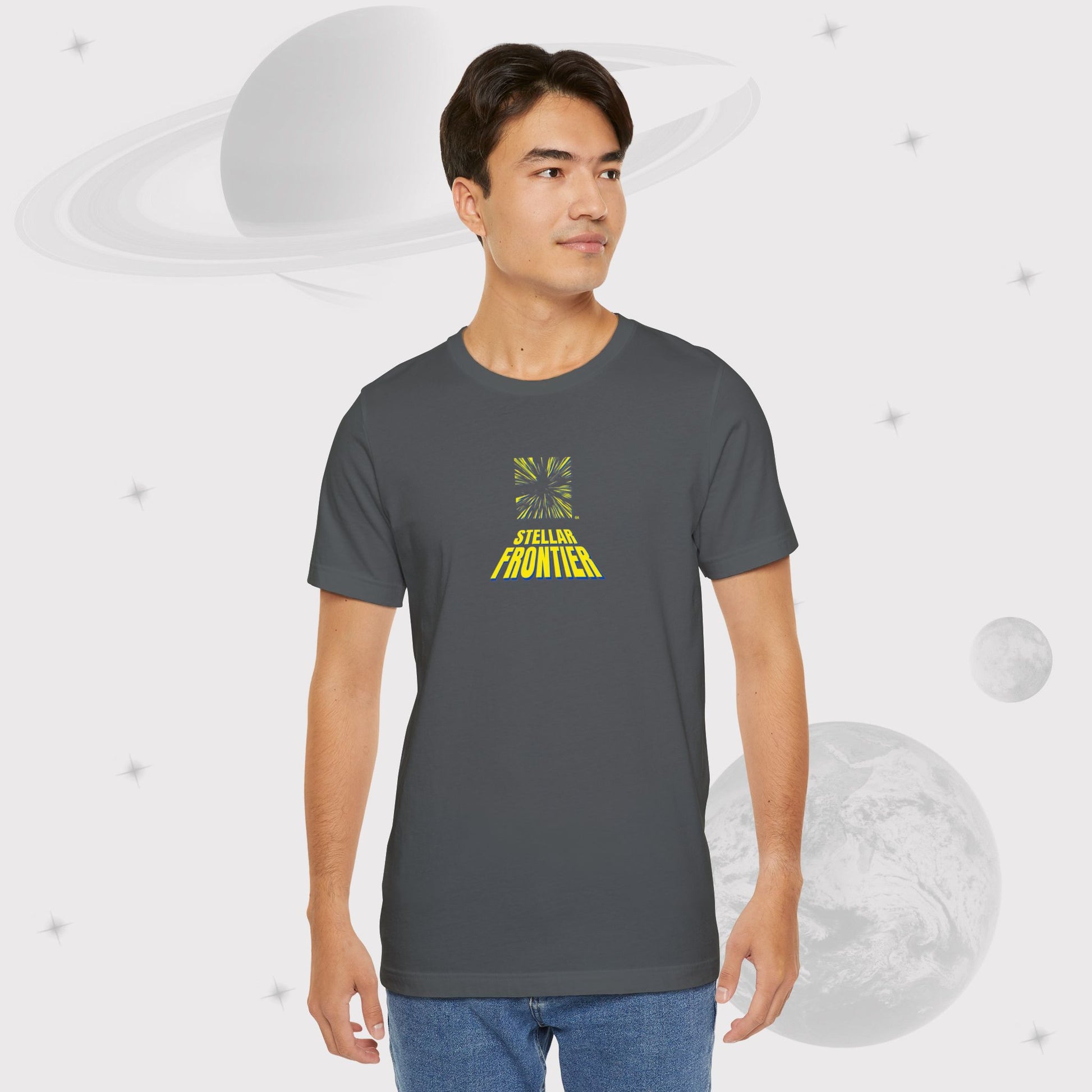 Guy wearing Going Across men's basic t-shirt in grey/asphalt, with jeans, featuring the text ‘Stellar Frontier’ and vibrant yellow, deep blue space art by Manharleen.