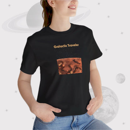 Woman wearing Going Across women's basic t-shirt in black, featuring the text ‘Galactic Traveler’ with space art of a red planet and a starry sky.