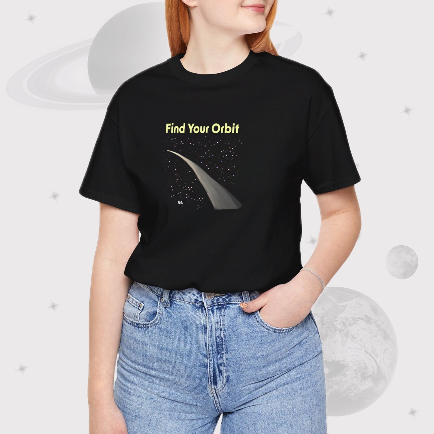 Woman wearing Going Across women's basic t-shirt in black with jeans, featuring the text ‘Find Your Orbit’ with space art of an orbit and a starry sky.